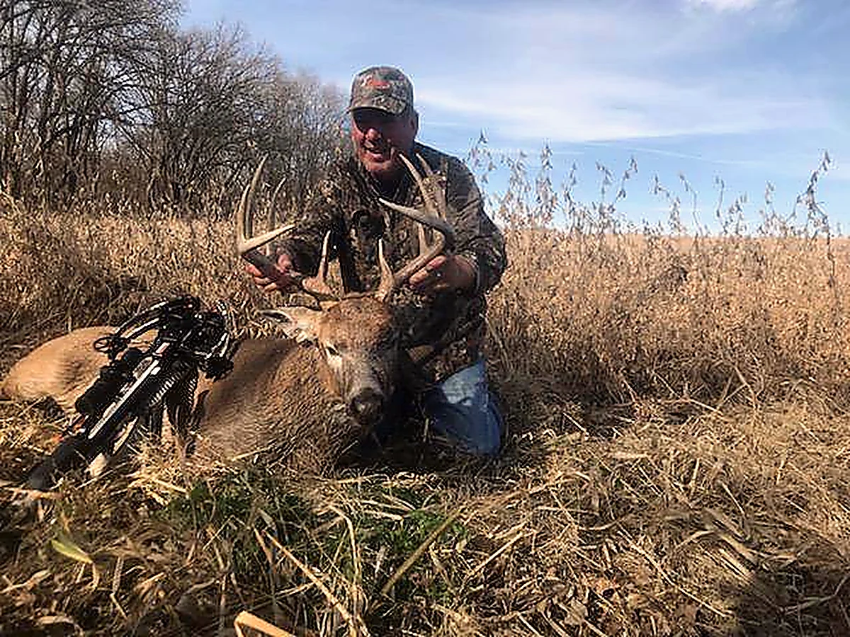 Hunter with a bow and an Illinois whitetail buck in a CRP field