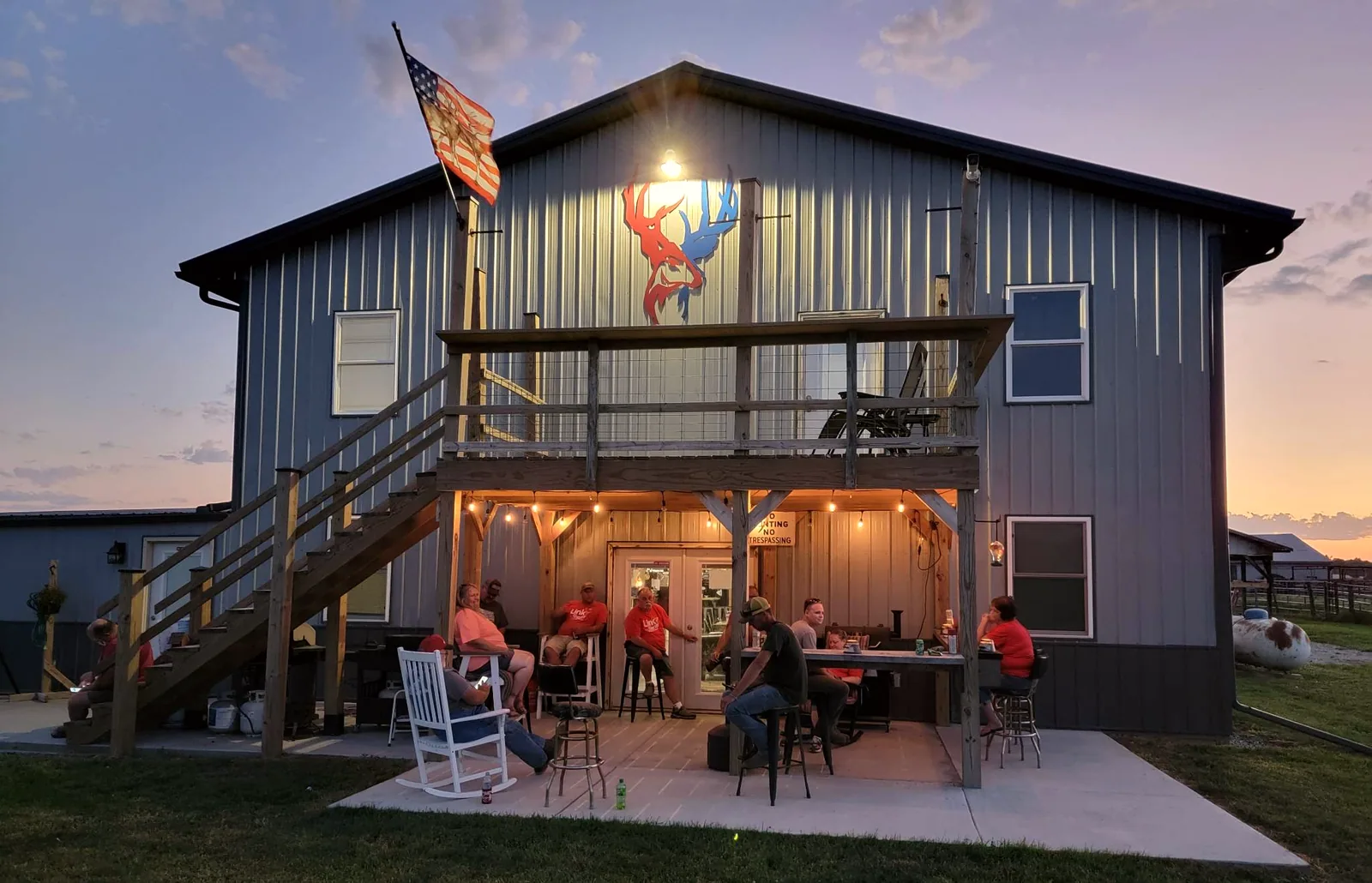 The Bigger Bucks Outfitters lodge lit at dusk with hunters on the deck in Media Illinois