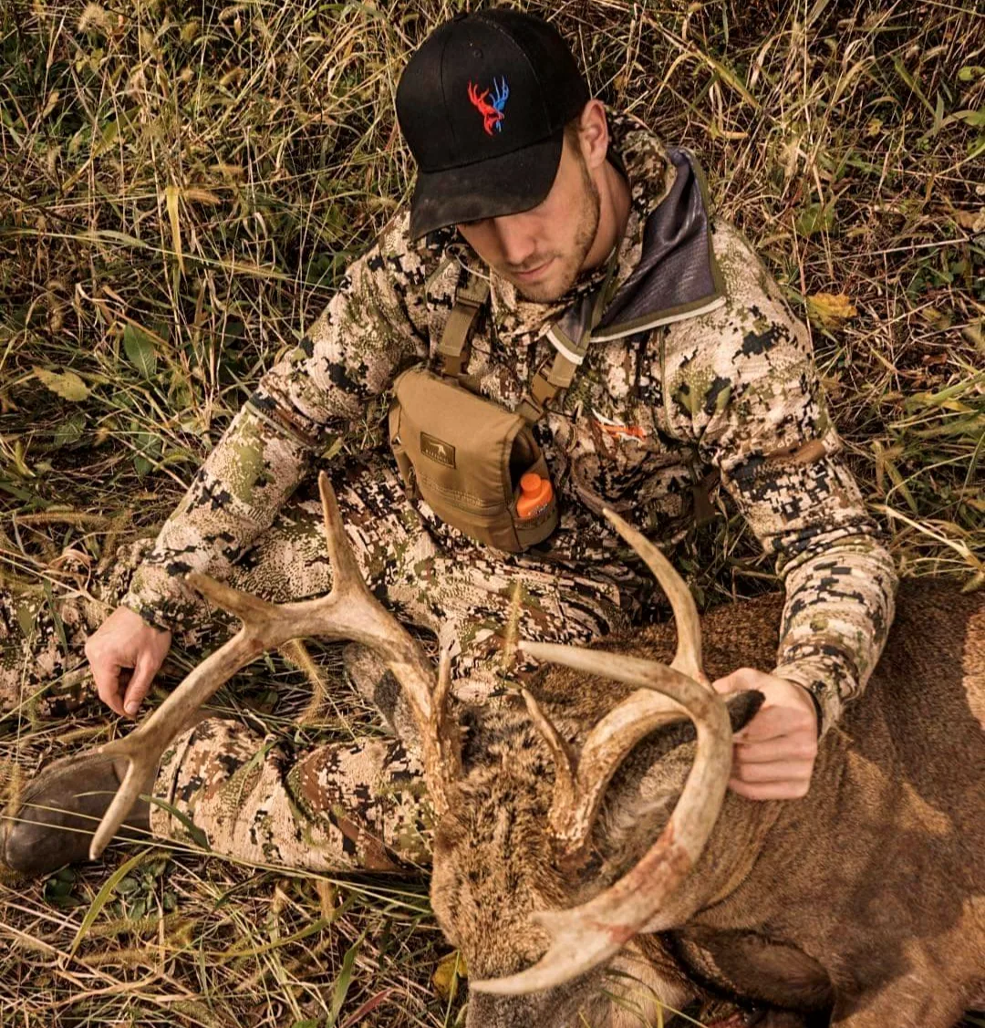 Hunter kneeling in tall grass with a heavy non typical whitetail taken at Bigger Bucks Outfitters