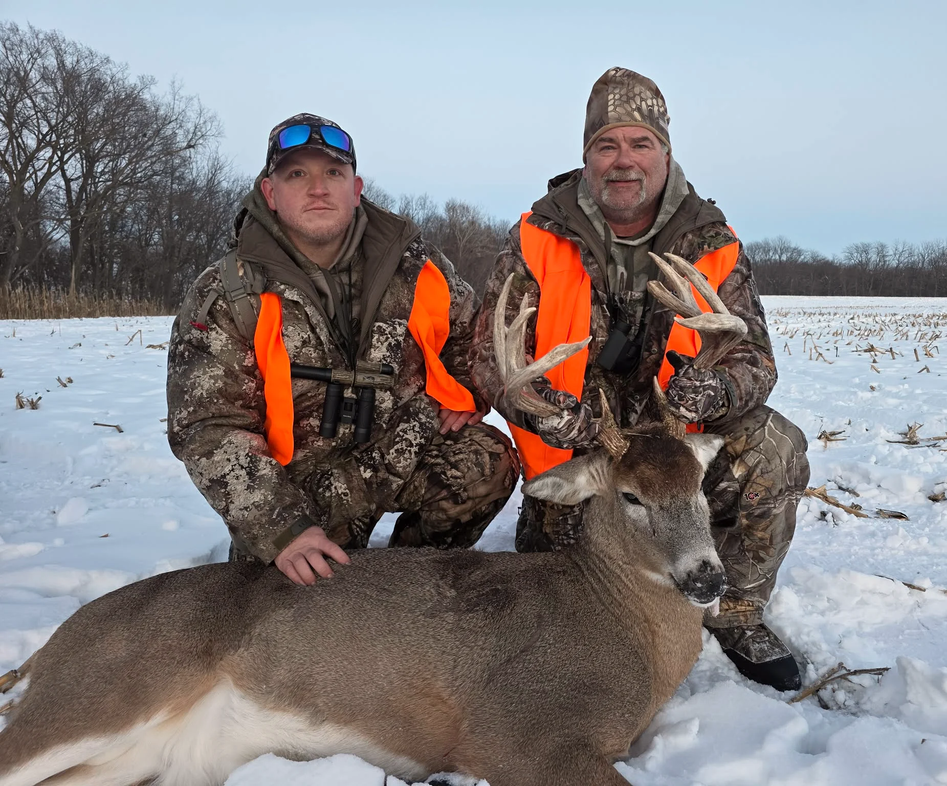 Hunters in blaze orange with a whitetail buck in the snow in Illinois